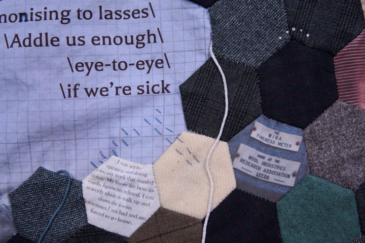Photo by Jonathan Turner @jonturner on Instagram of extract of artwork    
Left: On gridded paper printed on grey cloth part of a poem with phrases separated by back slashes and spaces:
…nonising to lasses\
 \Addle us enough\
             \eye-to-eye\
             \if we’re sick
Right and centre: Patchwork of hexagons in different materials and muted colours interspersed by patches of ephemera e.g., a patch that includes a label with the following text: The WIRA Fineness Meter and Made at the Wool Industries Research Association Leeds and another with:
I was set to spinning and doing jobs; any work that wanted doing. My knees are bent inward, ligaments relaxed. I can scarcely abide to walk up and down the room. Sometimes I am bad and am forced to go home. 
Blue stitches cross the gridded paper and some of the patchwork. 