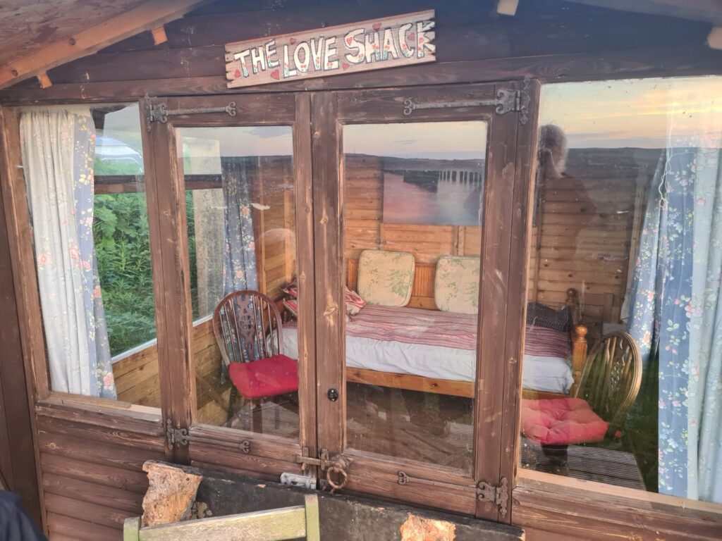 wooden hut with bed, chairs and windows on all sides.